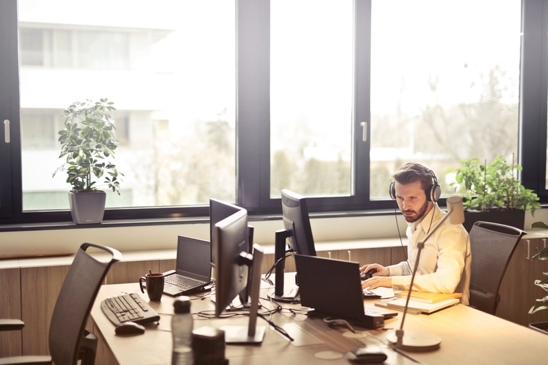 Mann sitzt am Schreibtisch mit Headset auf dem Kopf vor einem Bildschirm