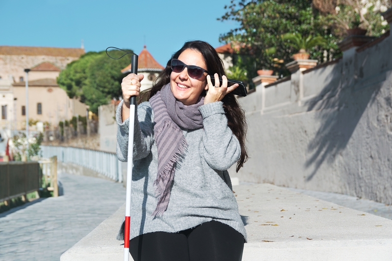 Eine blinde lächelnde Frau, die Voice-Over auf ihrem Smartphone benutzt.