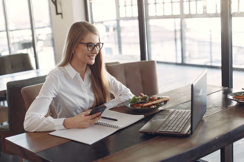 Frau sitzt mit Handy in der Hand am Tisch vor einem Laptop